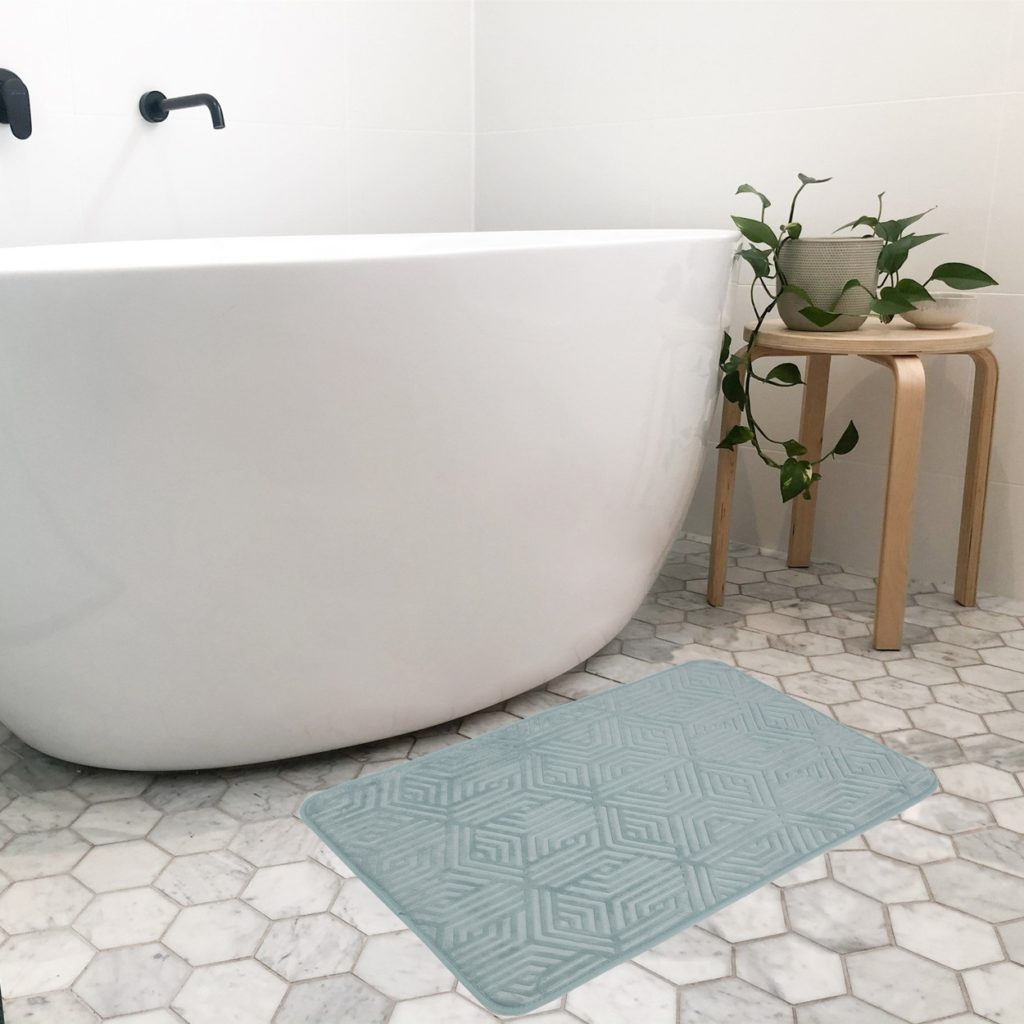 Teal coloured bath mat with geometric shapes set in a bathroom with large bath 