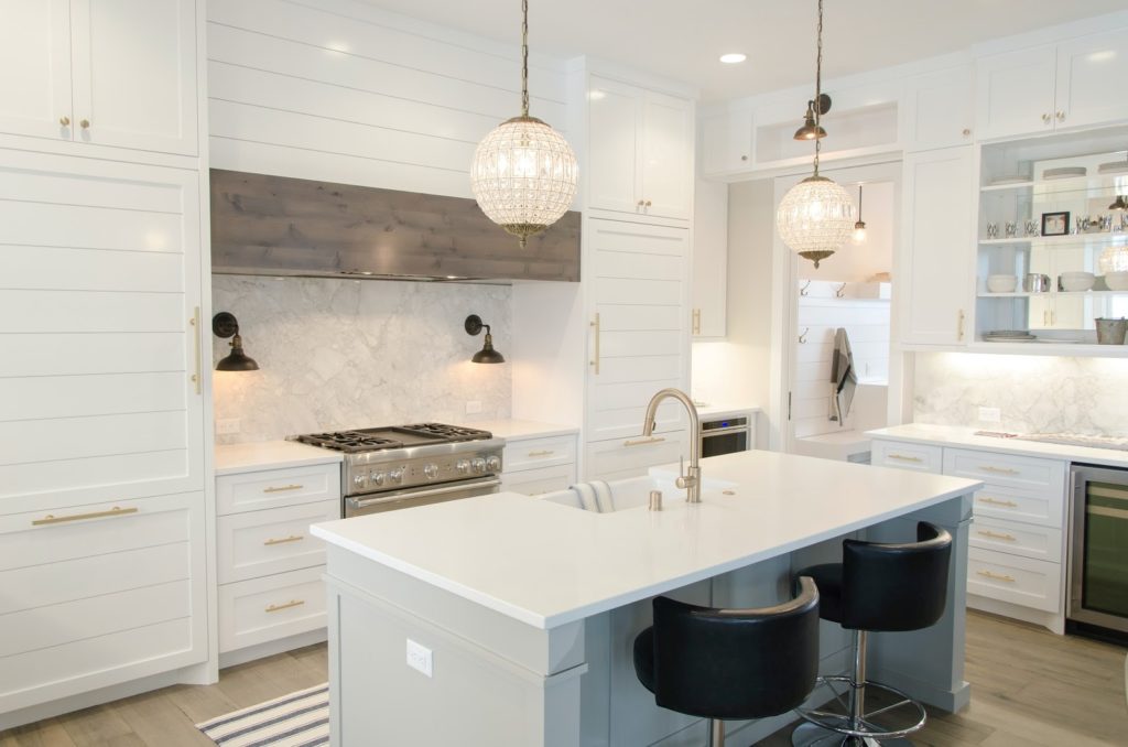 A bright white kitchen with decorative lights hanging above a kitchen island 