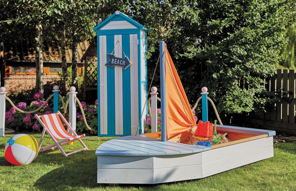 bright coloured boat shaped sand box, beach hut, beach ball and chair set in garden