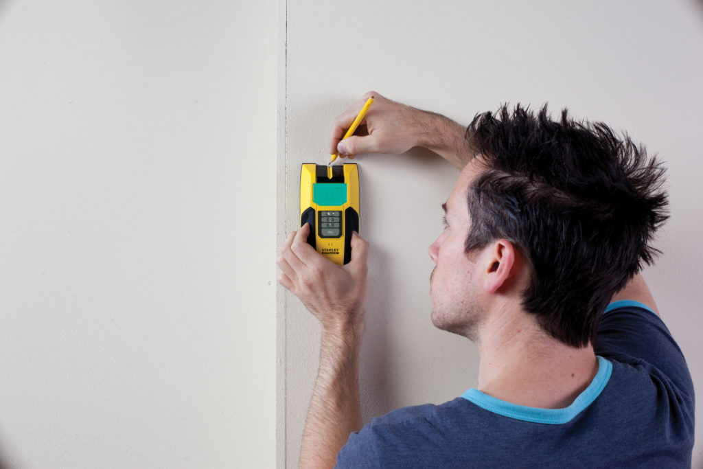 person holding stud detector and pencil against wall 
