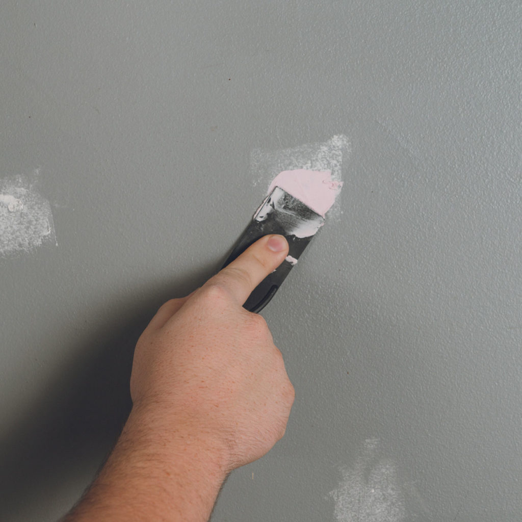 A filling knife being used to fill in a crack in the wall using multi purpose filler.