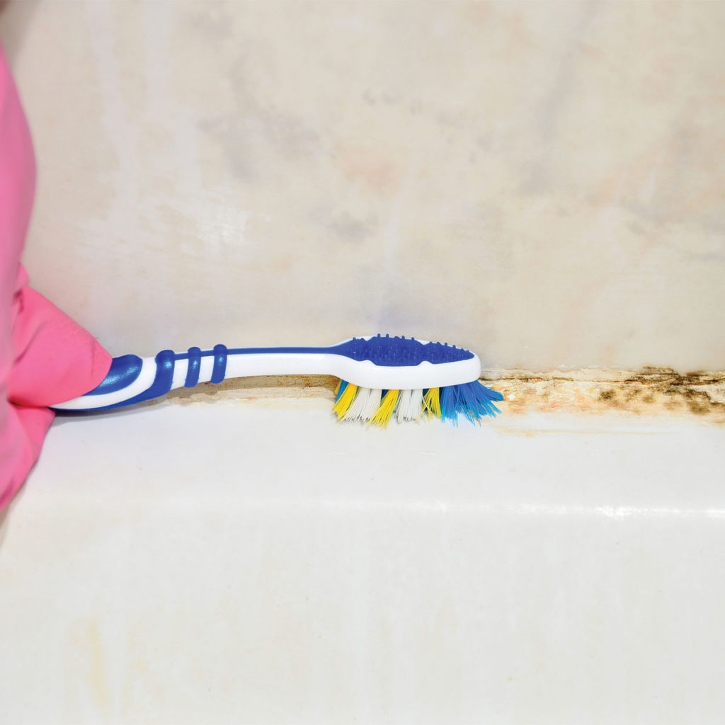 A person in a pink glove removing mould using a blue toothbrush.