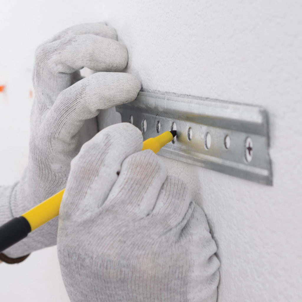 Plasterboard wall being marked with a pencil to prepare for drilling.