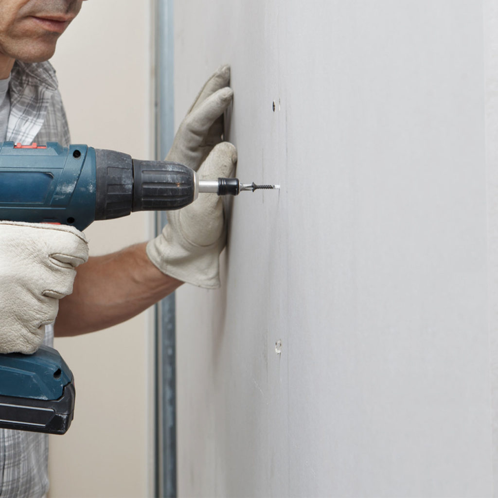 A man drilling into a plasterboard wall with a drill bit and blue power drill.