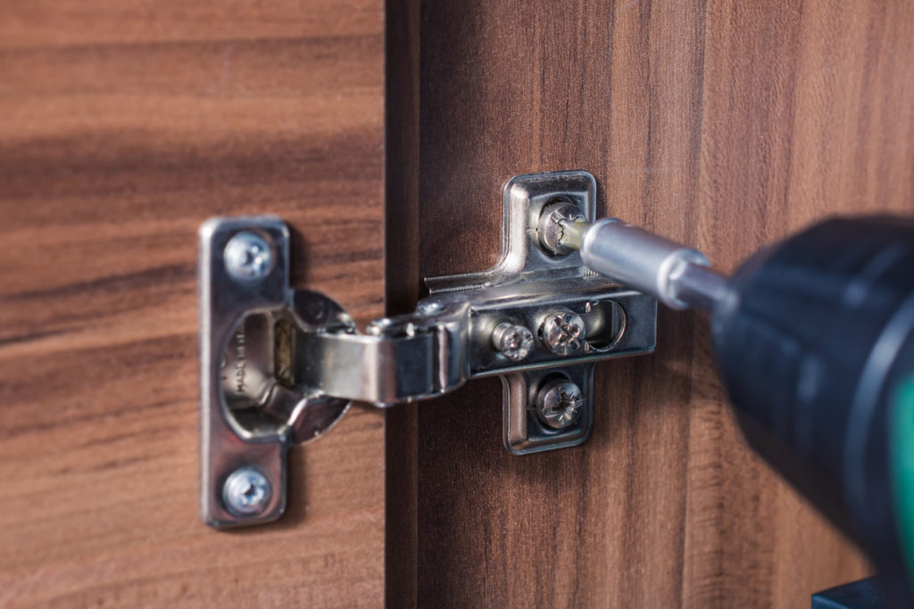 Close up of cupboard hinge with a drill screwing in screws