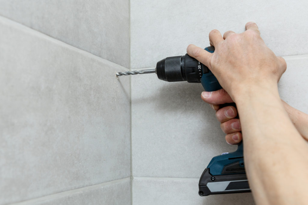 hand holding drill while drilling into tiled wall