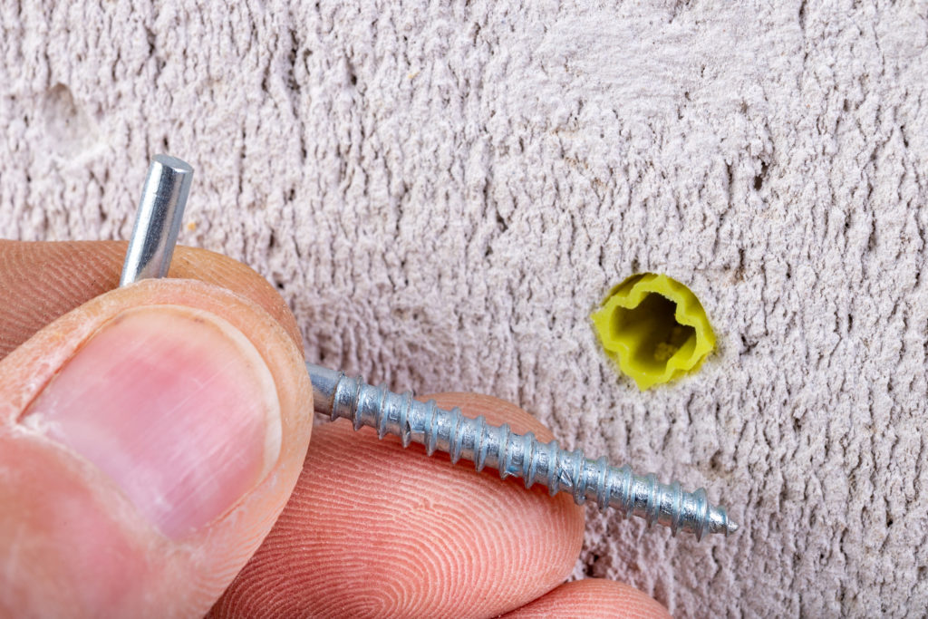 A rawl plug plasterboard fixing inserted into the wall, while a screw is going in to.