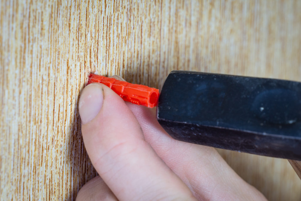 The male hand hammers the dowel into the wall with a hammer. Dowel is hammered into the wall, close-up.