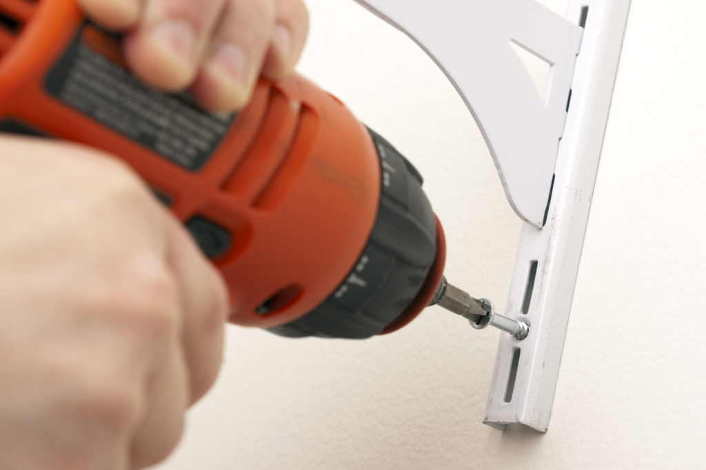 Using an electric screwdriver to mount a bracket for shelves on the wall. Focus on the screw.