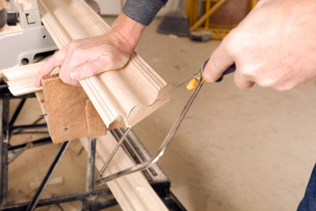 A man sawing the internal ends of a skirting board with a coping saw.