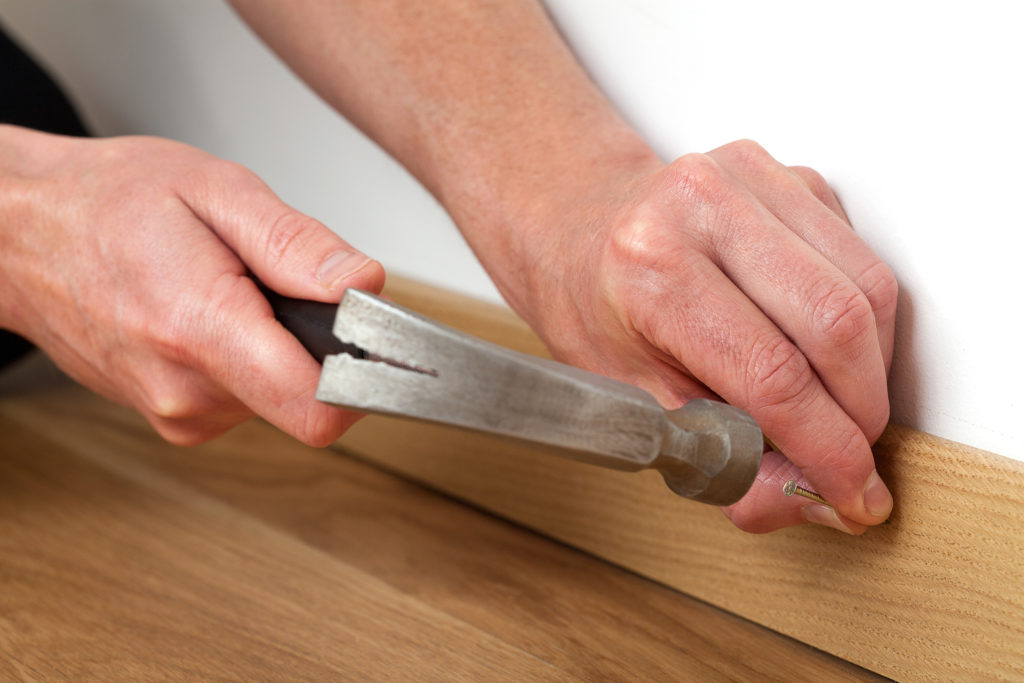 Man's hand hammering a nail into a skirting board.