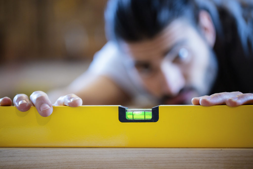 A young man using a yellow spirit level to make sure a shelf is level.