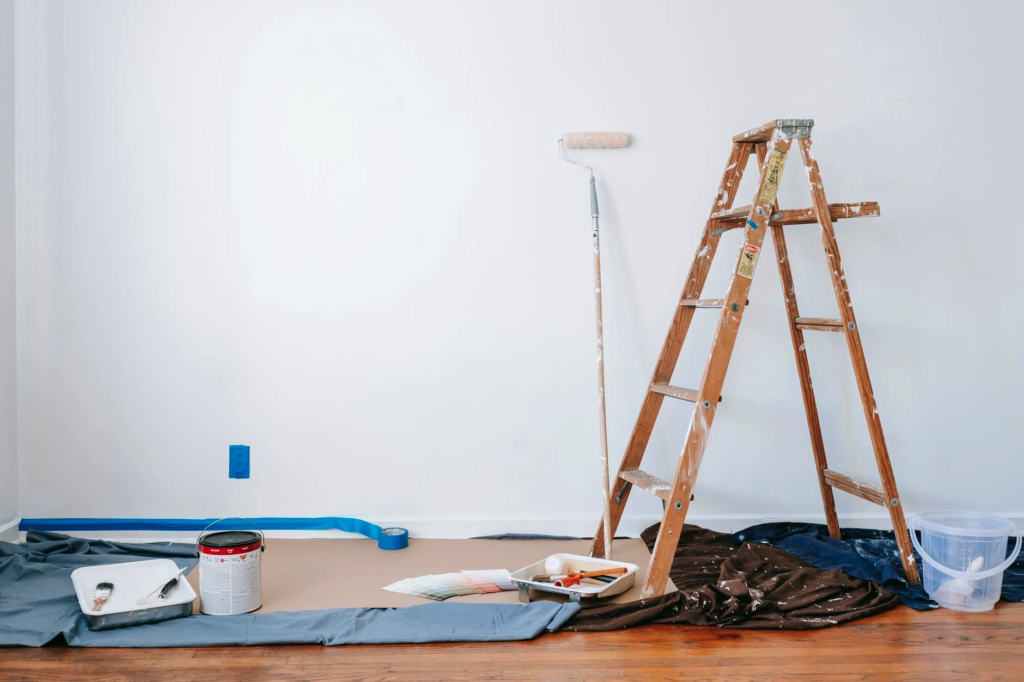 A step ladder with a long paint roller is set against a white wall, ready to use after the owner reads how to paint a ceiling guide.