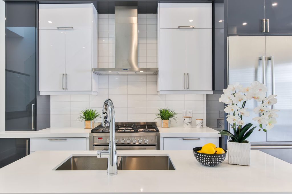 A crisp clean whte kitchen with a fruit bowl and flowers on the kitchen island