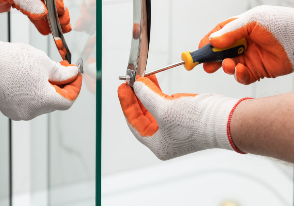 close up of hands wearing gloves screwing shower door handle in place with screwdriver