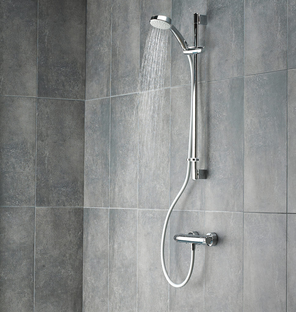 water coming through shower head, fixed on a grey wall in bathroom