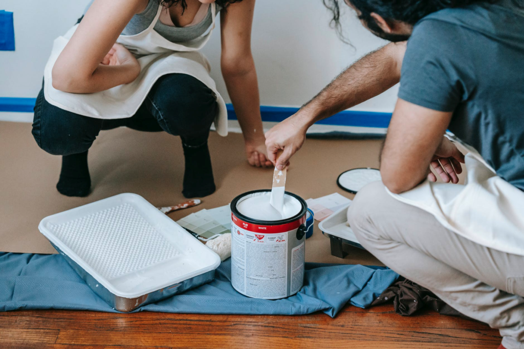 A man and woman kneel down to stir paint in a can as they prepare to paint a ceiling.