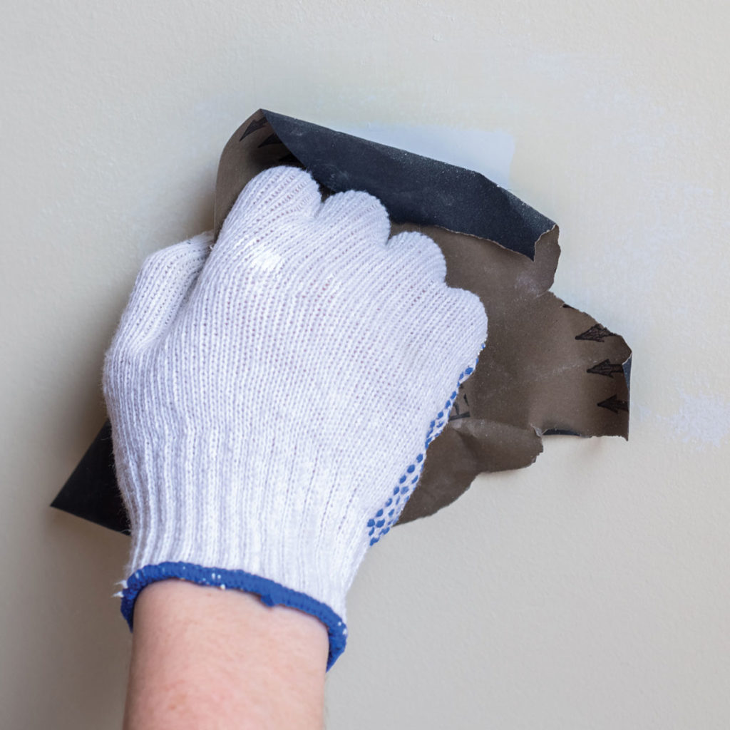 A hand sanding down a crack in the wall before they begin to fill it.