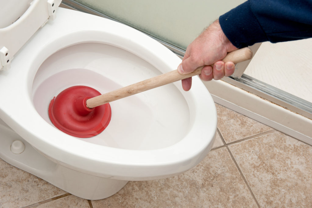 A man uses a plunger to unclog a toilet.
