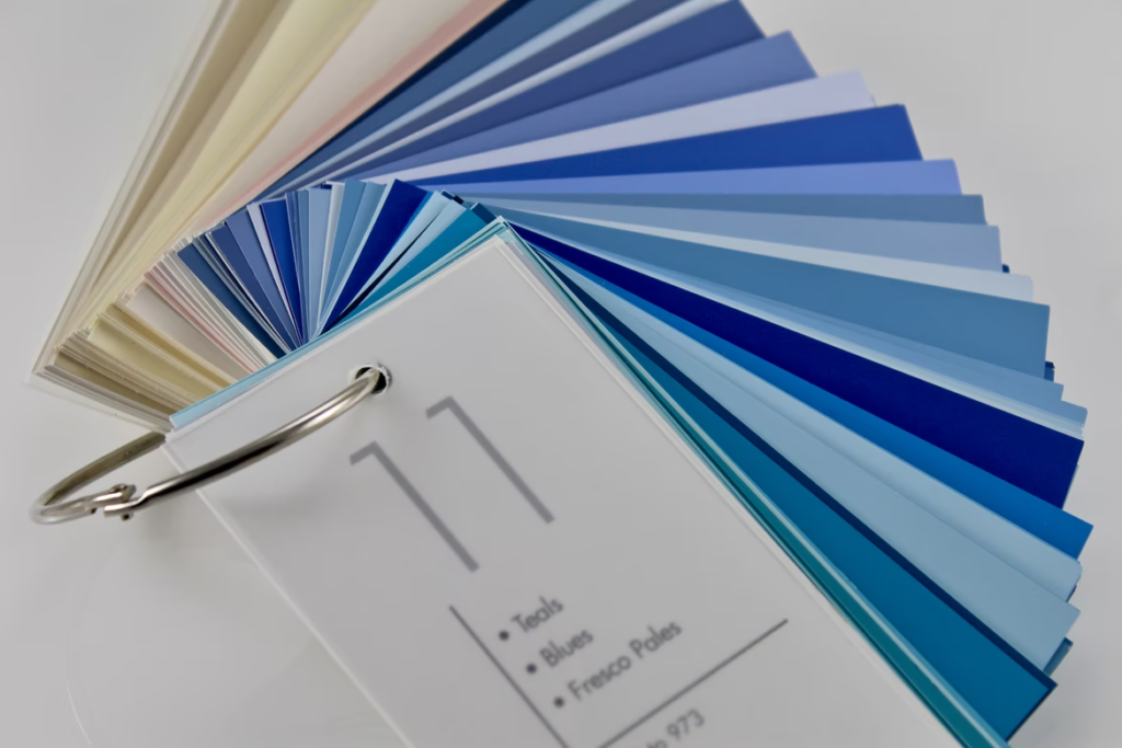 Blue paint colour swatches are laid out on a white table to help someone with how to choose paint colours.