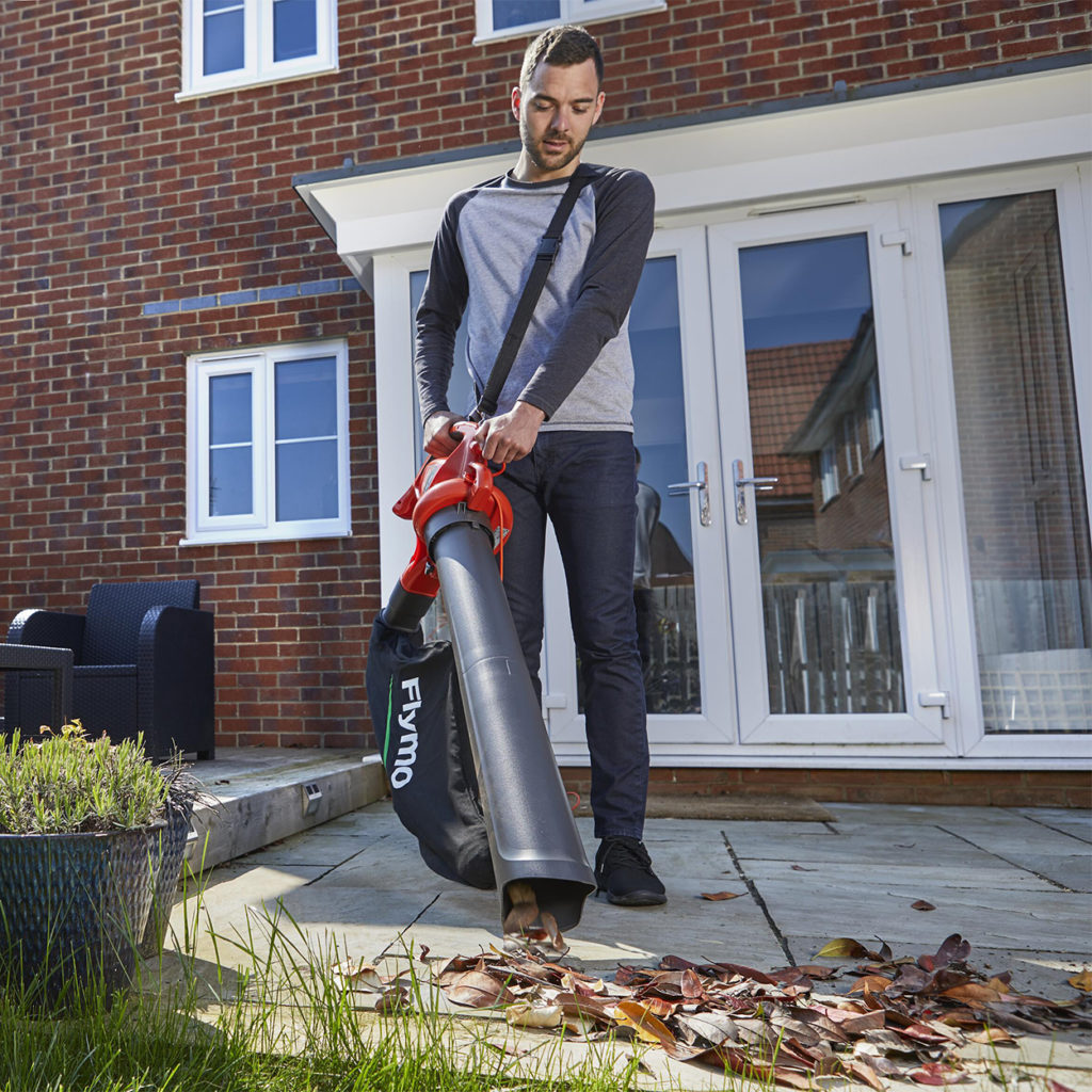 man using leaf blower to collect leaves in his garden