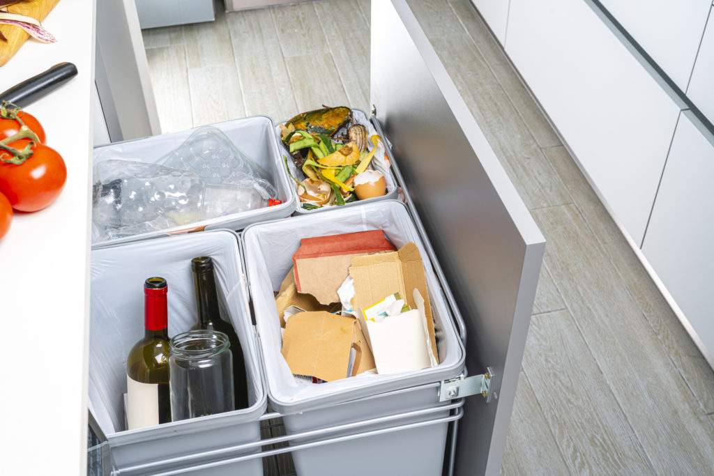 High angle view of an open modern kitchen cabinet with four garbage cans for glass, paper, plastic and organic waste
