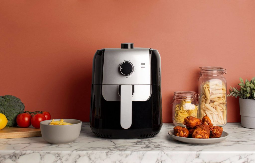 Air fryer sitting on kitchen counter with bowls and plates of food around