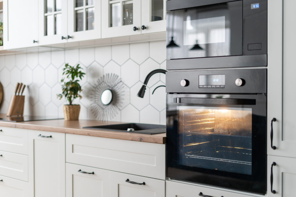 Side view of contemporary black oven kitchen interior design. Stylish white wood furniture surface with appliances and decor