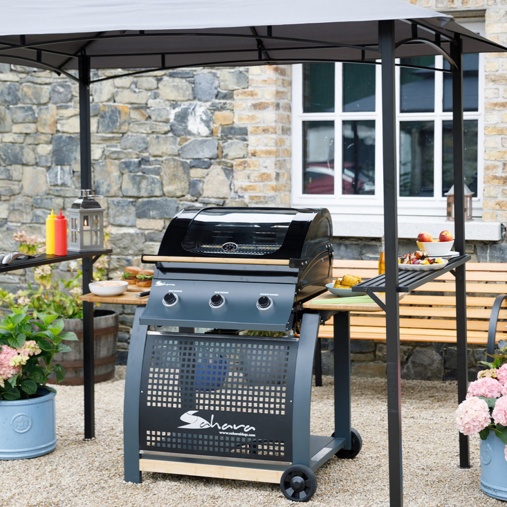 Gas BBQ set up under BBQ gazebo with food and accessories in garden