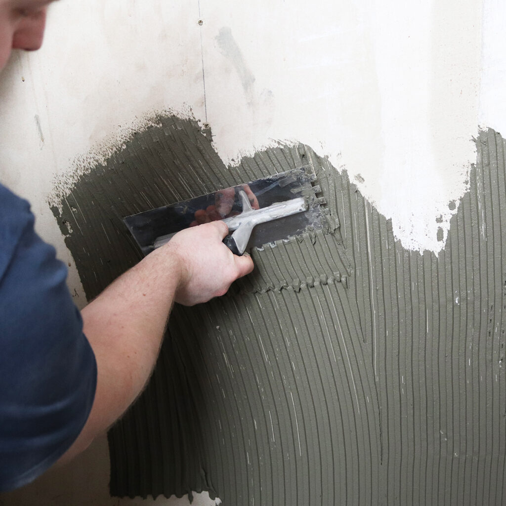 A man using a Vitrex notched trowel to spread adhesive