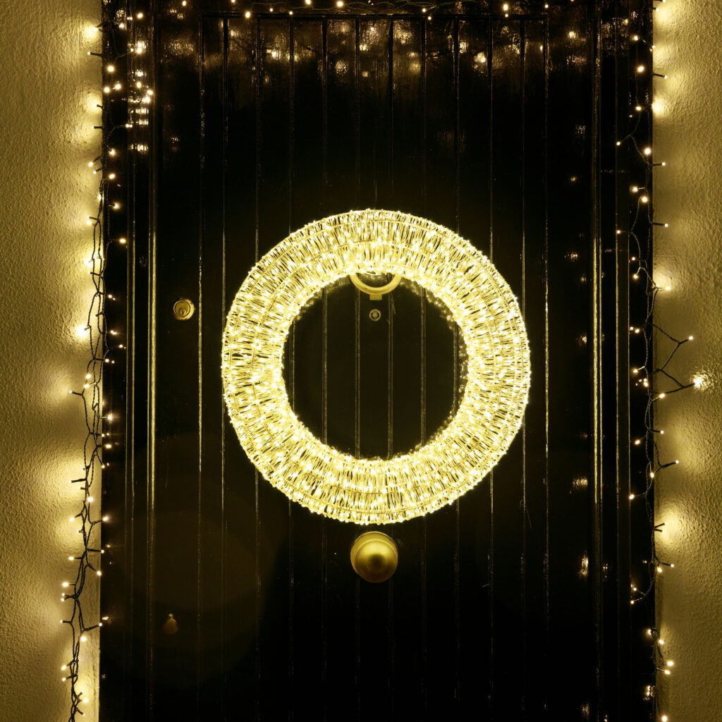 An image showing a front door lit up with Christmas lights
