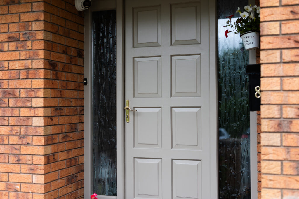 Finished front door painted soft grey, with decorative glass side panels and brass hardware.