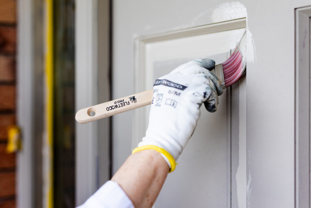 Using a paintbrush to paint the recessed edges and moulded details of a front door.