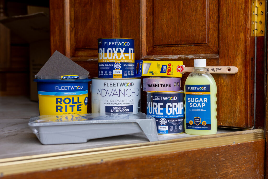 Front door painting supplies, including primer, paint, sugar soap, sandpaper, masking tape, brushes, a roller and tray