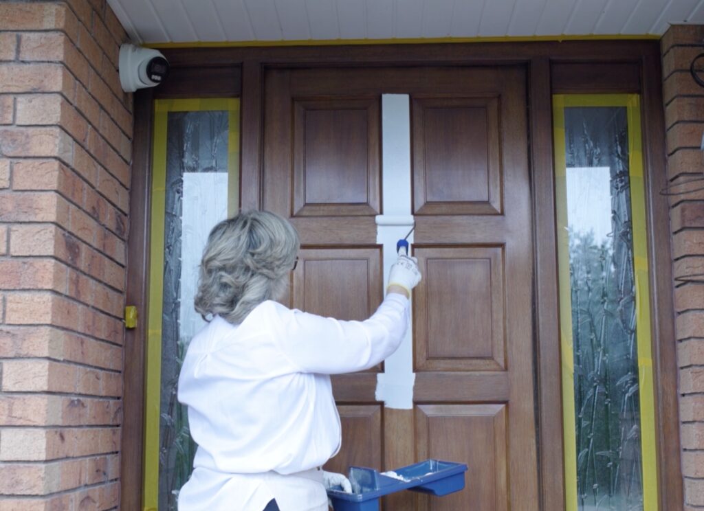 Applying white primer to the centre of a wooden front door with a small roller.
